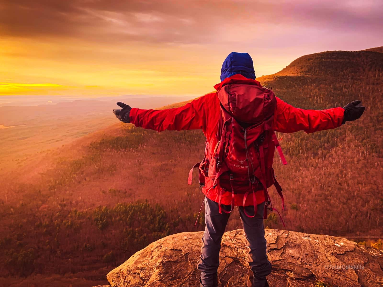 hiker with extended arms welcomes the sun from a mountain ledge